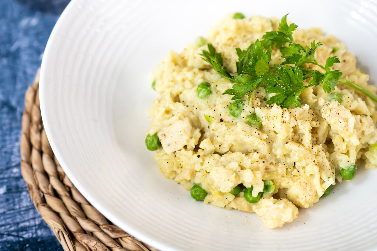 A close-up shot of creamy Caribbean curry with green peas and parsley, served on a white plate over a woven placemat.