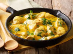 Chicken curry in a black skillet on a wooden surface with a yellow napkin.