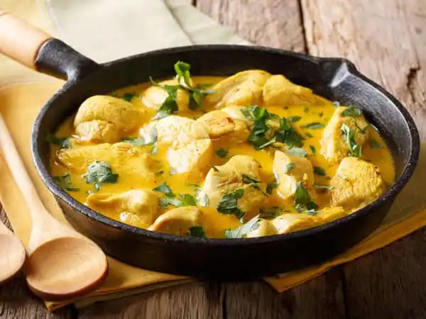 Chicken curry in a black skillet on a wooden surface with a yellow napkin.