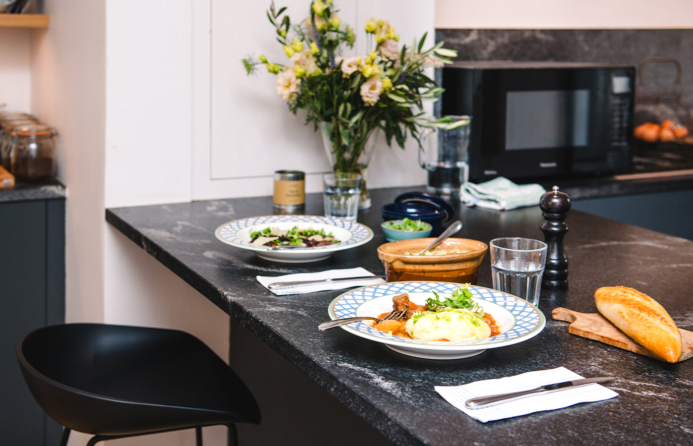 Kitchen counter with plates of food, glasses, and a vase of flowers.